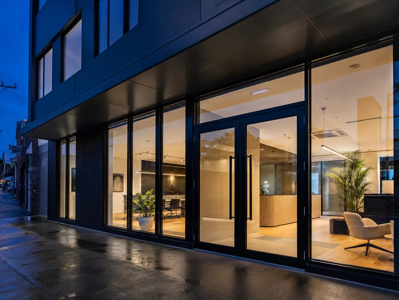 Completed glass shopfront entry with heavy-duty aluminium commercial framing, lit from inside at dusk